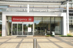 Entrance of an emergency department with glass doors and a red sign displaying a white cross.