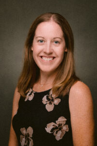 Person smiling in a professional portrait against a dark background.