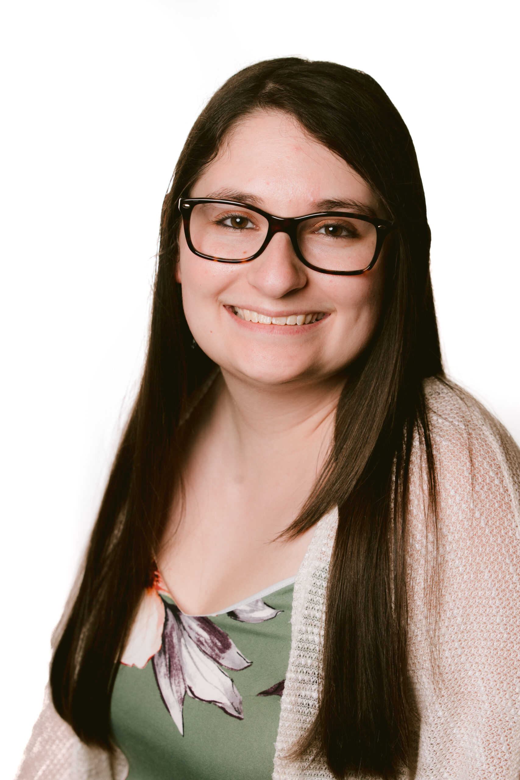 Person with long dark hair and glasses smiling in a portrait against a white background.