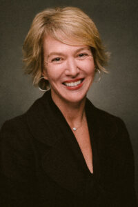 Person smiling in a black jacket against a dark background.