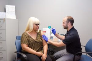 Healthcare professional administering a vaccine to a seated patient in a clinic room.