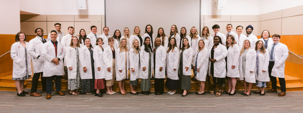 A diverse group of professionals, wearing white coats, pose in rows for a formal group photo.