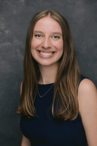 Professional headshot of a person with long straight hair wearing a navy sleeveless top.