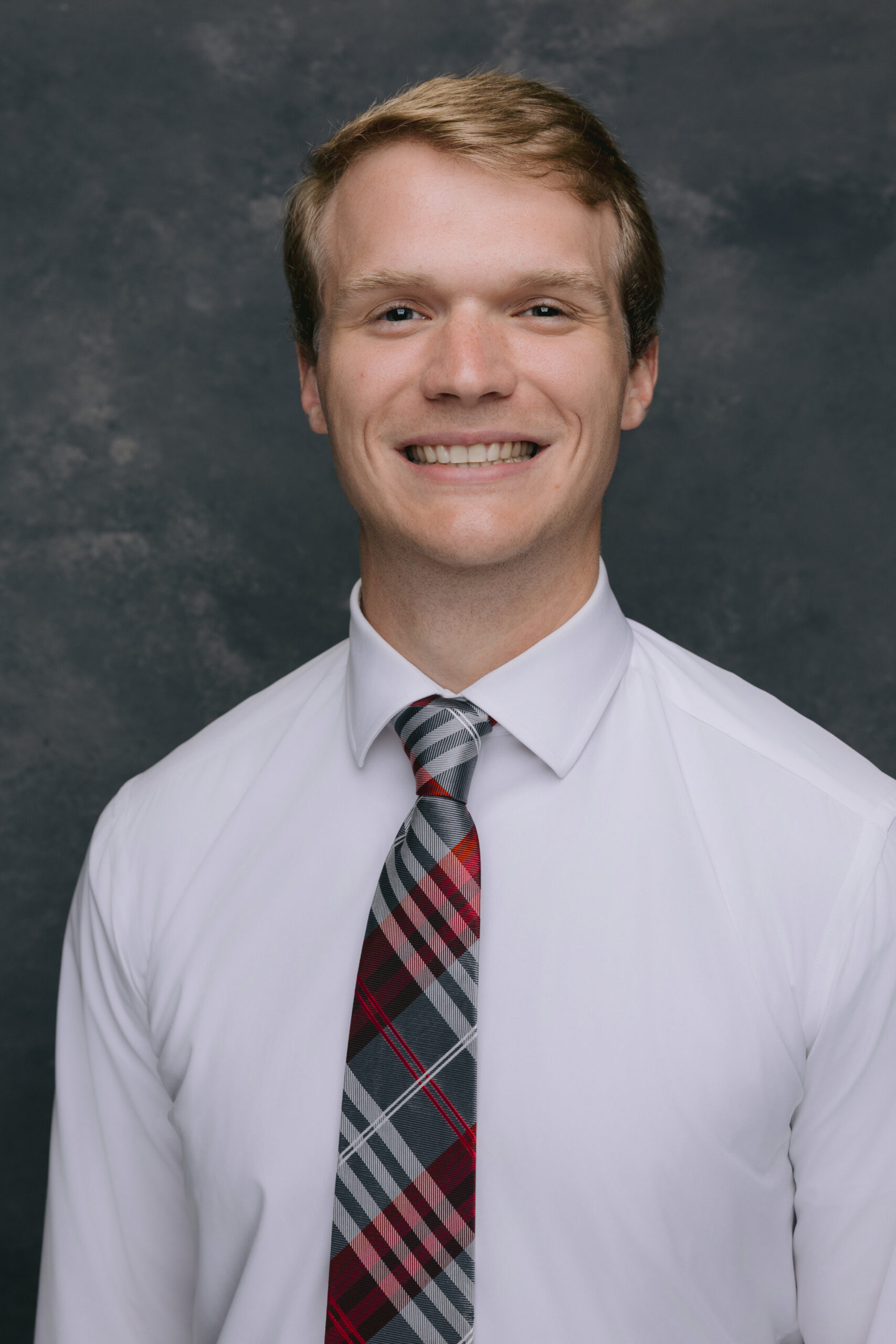 Professional headshot of a person wearing a white shirt and plaid tie.
