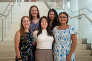 Five people pose on an indoor staircase in a modern building for a group photo.