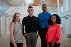 Four people pose together on an indoor staircase in a modern building.